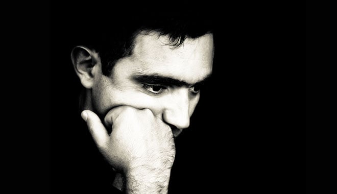 Black and white  dramatic close-up  of a man thinking with a fist on his chin emerging from a black background