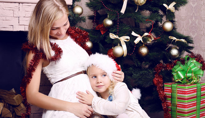 adorable photo of happy family. pregnant mother with her little cute daughter posing beside a decorated Christmas tree and presents