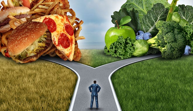 Diet decision concept and nutrition choices dilemma between healthy good fresh fruit and vegetables or greasy cholesterol rich fast food with a man on a crossroad trying to decide what to eat for the best lifestyle choice.